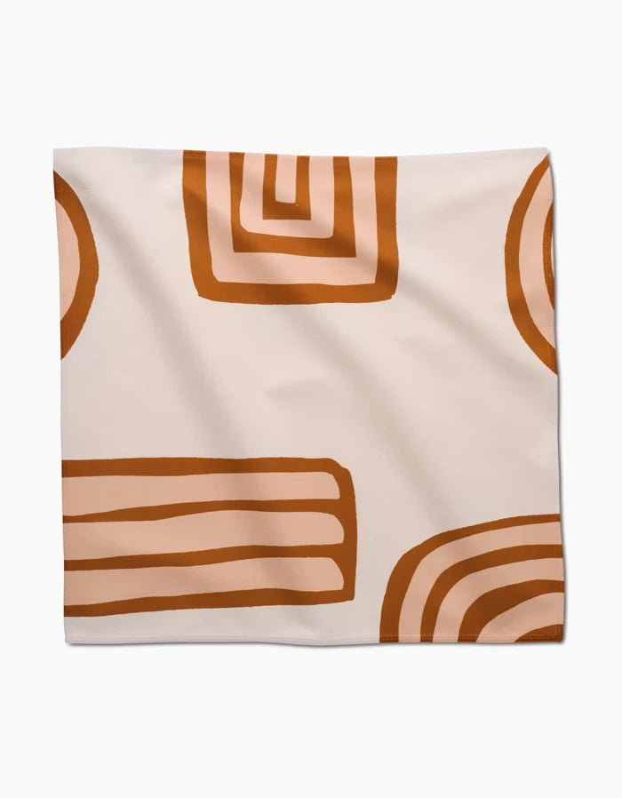 The GEOMETRY Terracotta Vibes napkin features a cream background with abstract brown and orange geometric shapes, such as rectangles, half-circles, and concentric lines.