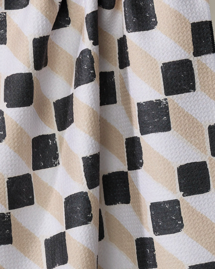 A close-up of Tessera by Studio Jeannot shows textured fabric with alternating black squares and beige diamonds on white, perfect as a stylish kitchen towel made from recycled materials.