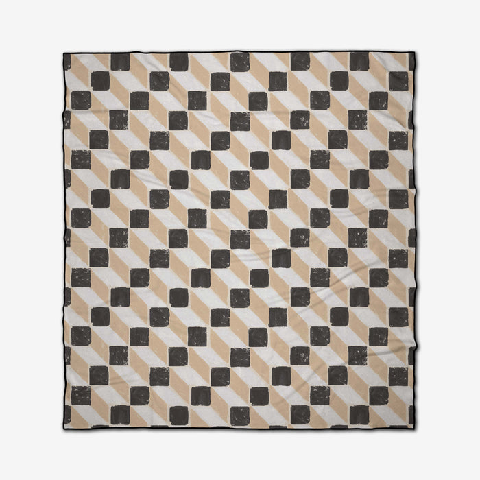 The Tessera Beach Blanket by Studio Jeannot features a square design with beige, black, and white geometric cubes and rectangles for a 3D effect. Made from quick-drying recycled materials for eco-friendly comfort.