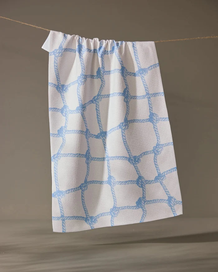The Geometry Tethered Blue ultra-absorbent dish towel, featuring a blue rope knot pattern on white, hangs from a beige string against a neutral background.