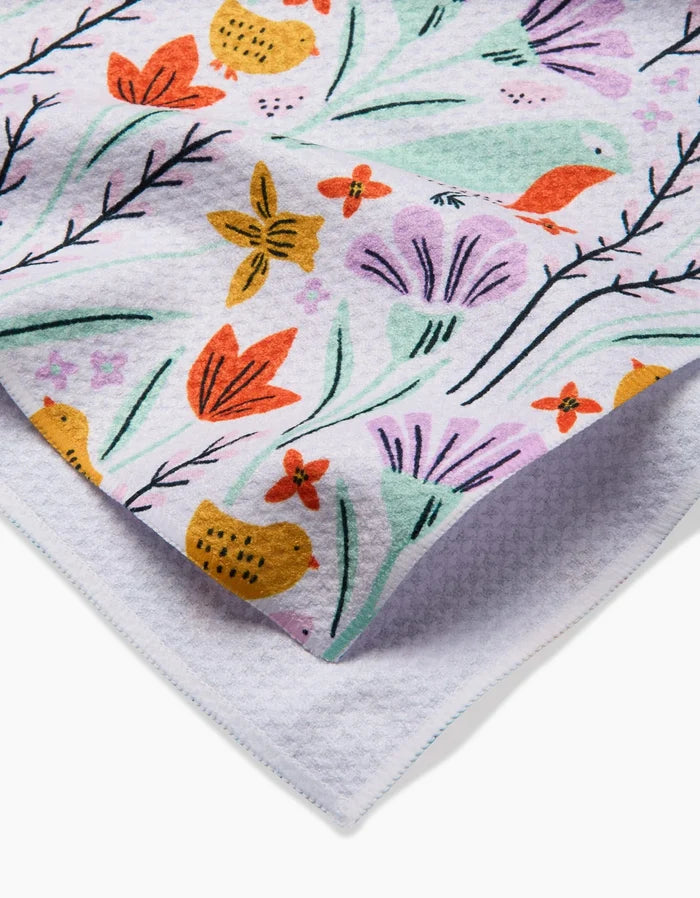 A close-up of the Thaddeus tea towel by Amy MacCready, featuring a colorful botanical print with flowers, leaves, and small birds. A folded corner shows the ultra-absorbent textured underside.