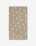 The Thatcher rug by Studio Jeannot is a rectangular beige rug with a geometric checkerboard of small squares and parallel brown lines, made from recycled materials. Shown on a white background.