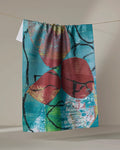 Katherine Berkeley’s “The Apple Doesn’t Fall Far From the Tree” tea towel features a colorful abstract design with red shapes, black lines, and a blue-teal background, made from recycled materials and perfect for brightening your kitchen.