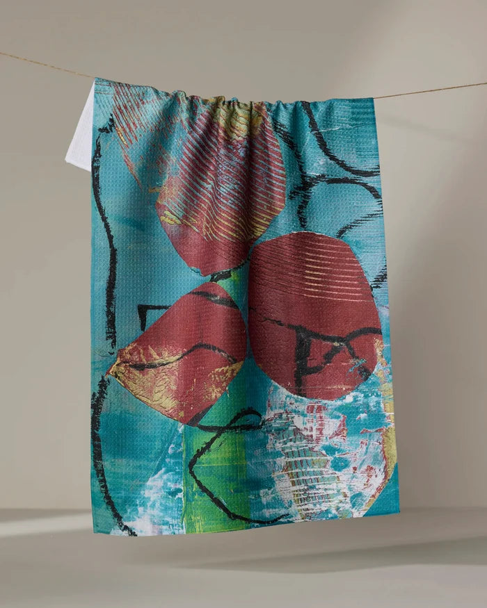 Katherine Berkeley’s “The Apple Doesn’t Fall Far From the Tree” tea towel features a colorful abstract design with red shapes, black lines, and a blue-teal background, made from recycled materials and perfect for brightening your kitchen.