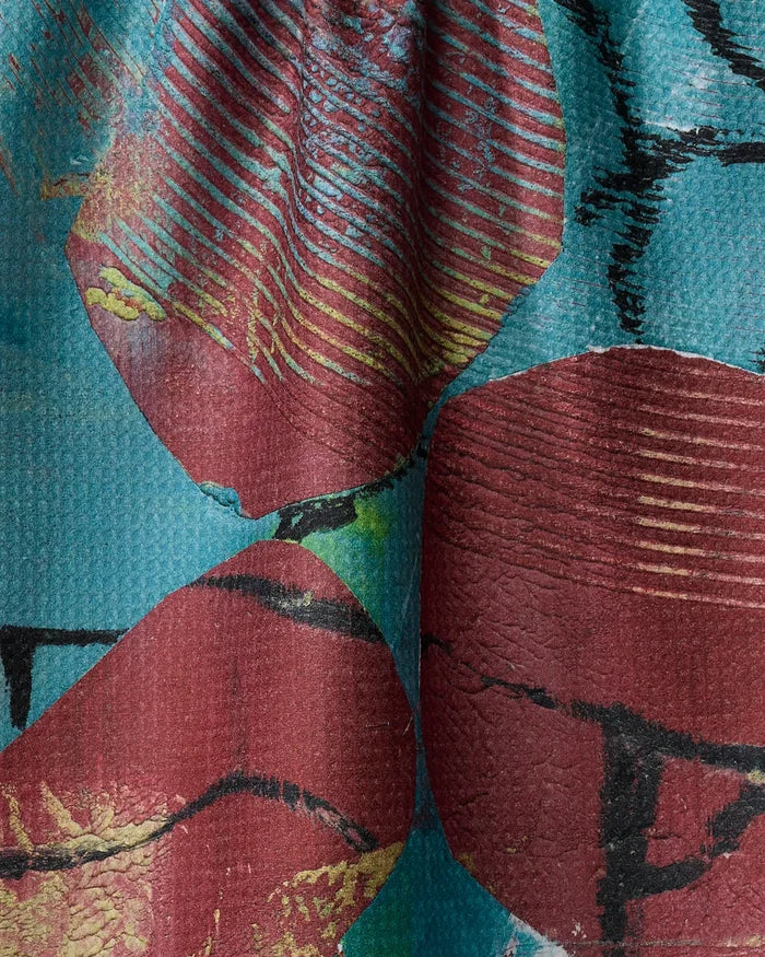 A close-up of Katherine Berkeley’s "The Apple Doesn’t Fall Far From the Tree" ultra-absorbent recycled tea towel, featuring large abstract red shapes with yellow accents on a turquoise background and intersecting black lines.