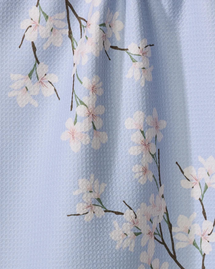 The Eve by Becki Owens is a light blue Geoweave tea towel adorned with white cherry blossom branches and pink centers, made from recycled materials.