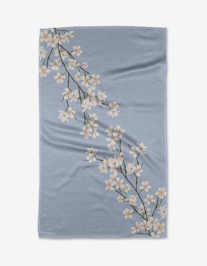 The Eve by Becki Owens is a light blue Geoweave™ blanket with two white cherry blossom branches, green leaves, and brown stems, crafted from recycled materials.