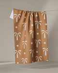 The Perfect Palm tea towel by Elizabeth Edwards features a white palm tree and star pattern on brown. Made from ultra-absorbent material, it’s both stylish and practical—a charming addition to any home.