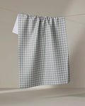 The Jenny Keller Tidepool Check kitchen towel in blue and white checkers hangs on a clothesline against a plain, neutral background.