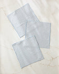 Three Tidepool Check dishcloths by Jenny Keller, featuring a light blue and white houndstooth pattern, are neatly displayed on a white marble surface with subtle beige veining.