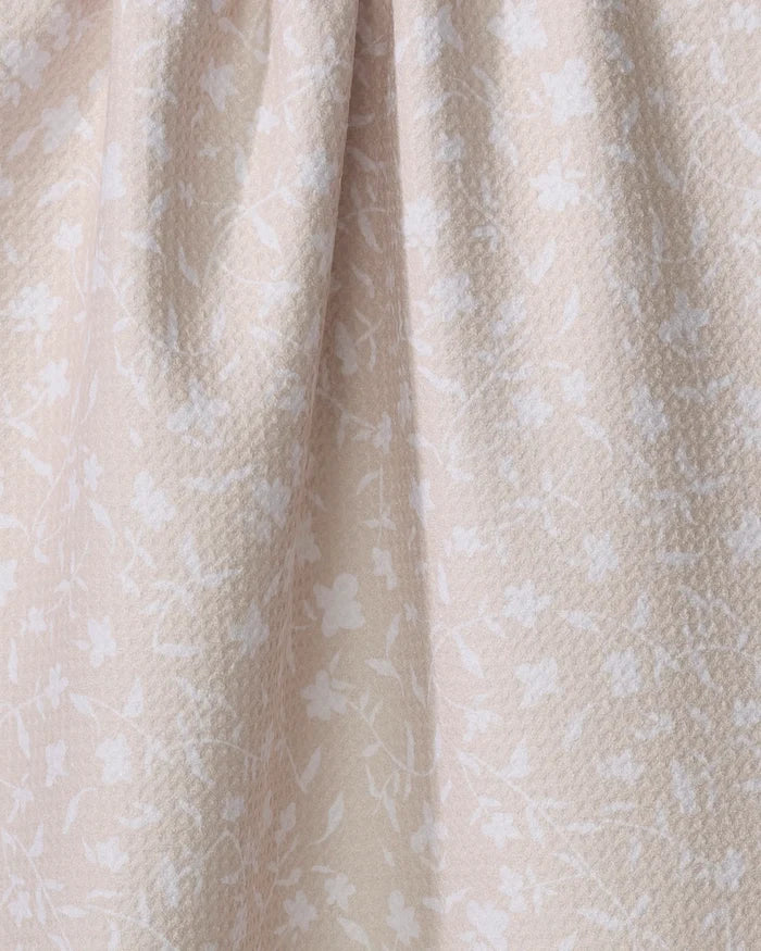 Close-up of the Aubrey Fairchild Tiny Floral tea towel in beige, featuring a subtle white floral pattern and gentle folds. Made from ultra-absorbent recycled materials for style and sustainability.