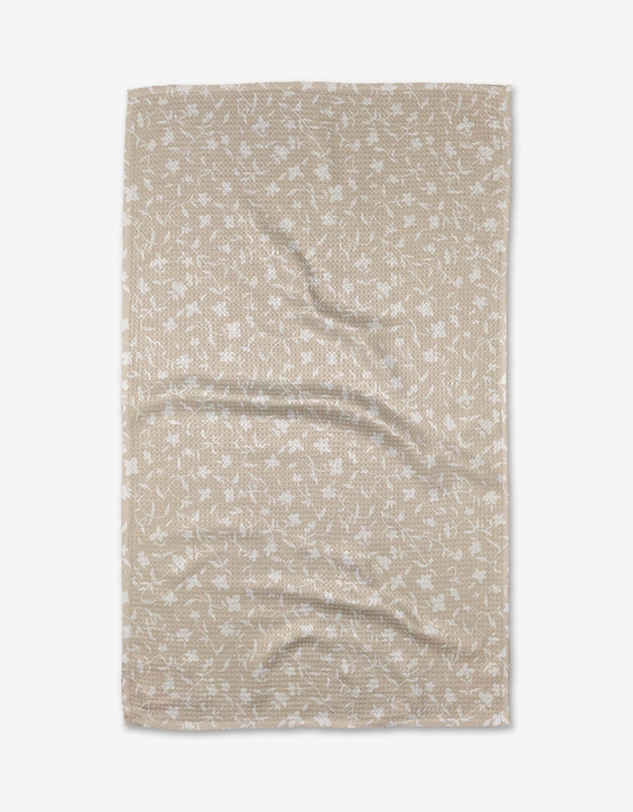 The Tiny Floral bath towel by Aubrey Fairchild is beige and rectangular, made from Geoweave fabric with a subtle white floral pattern, shown flat with gentle creases.