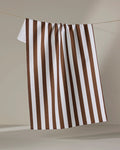 The Kailee Wright Toni Stripe tea towel, featuring white and brown vertical stripes and made from recycled materials, hangs on a string against a neutral background.