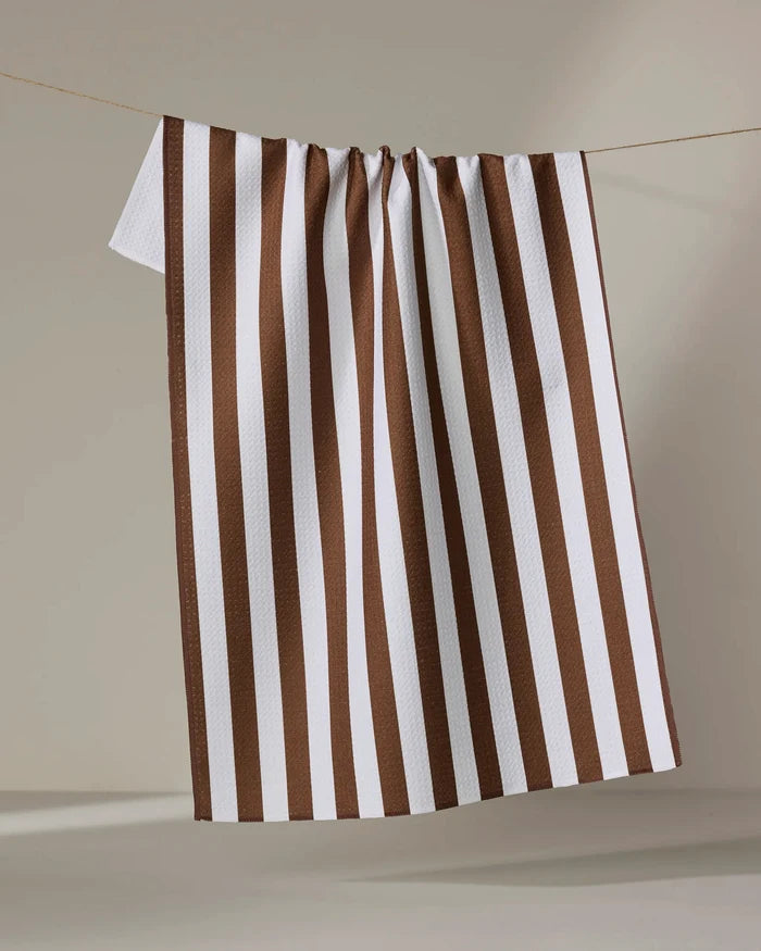 The Kailee Wright Toni Stripe tea towel, featuring white and brown vertical stripes and made from recycled materials, hangs on a string against a neutral background.