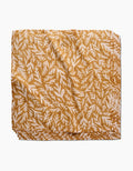 The Trail Dusting Gold napkin by Twig + Spark features an absorbent, golden yellow cloth with a white leafy branch pattern, neatly folded and stacked on a plain white surface.