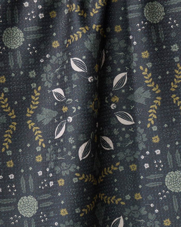 The Ash Cascade Trailhead towel features ultra-absorbent dark fabric adorned with green, yellow, and white botanical patterns in symmetrical, finely detailed arrangements for a natural, intricate look and soft drape.