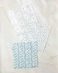 Three "Trailing Farmhouse Florals" napkins by Teri the Butter, featuring white and light blue botanical patterns and made from recycled materials, are arranged on a light marble surface.