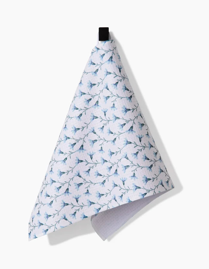 The Trailing Flowers in Blue kitchen towel by Teri the Butter, made from Geoweave fabric, features a blue floral pattern on white and hangs from a black loop against a white background.
