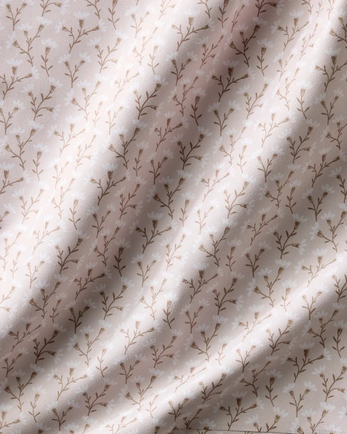 A close-up of Teri the Butter’s Trailing Flowers in Pink napkins, featuring soft, light pink recycled fabric with a delicate brown vine and leaf pattern and gentle highlights on their eco-friendly surface.