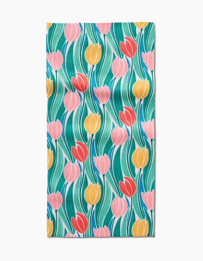 The Tranquil Tulips bar towel by Sarah Daugherty is made from Geoweave fabric and features a colorful tulip pattern with pink, red, and yellow blooms plus green leaves on a white background.