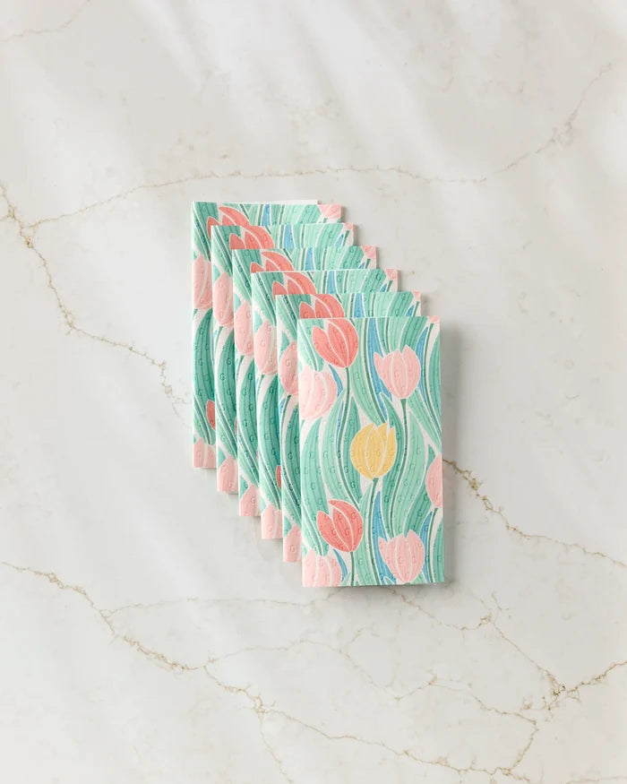 Six Tranquil Tulips rectangular reusable paper towels by Sarah Daugherty, featuring a pastel tulip pattern in pink, yellow, and green, are stacked neatly and offset on a marble surface.