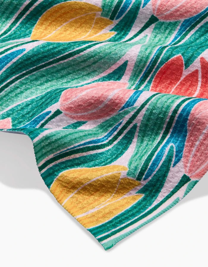 A close-up of the Sarah Daugherty Tranquil Tulips bar towel, made from Geoweave fabric and featuring a floral design with yellow and pink tulips, green leaves, and flowing blue accents on a white background.