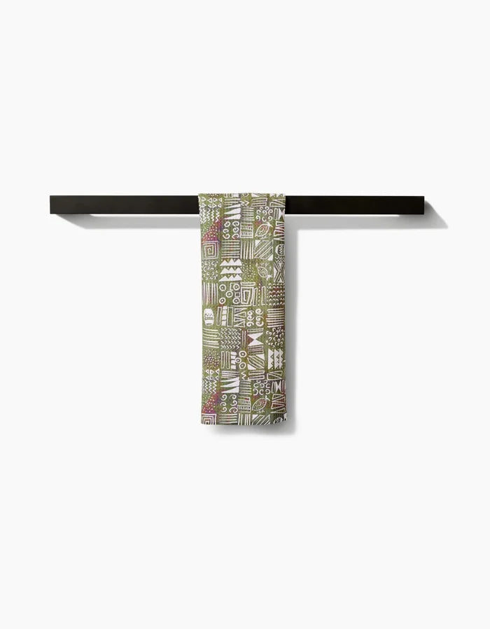 The Tribal Symbols bar towel by Taryn Brennan, featuring abstract green and white patterns on eco-friendly Geoweave fabric, hangs neatly folded over a dark horizontal rack against a plain white background.