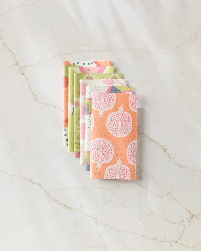 A stack of five folded Lizzie Clark Tropical Fruit reusable paper towels with pastel pomegranate, dot, and abstract designs rests on a white marble surface with light brown veining.