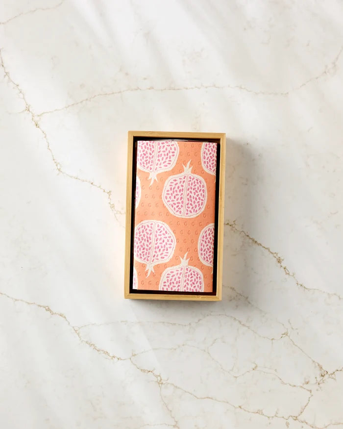 A rectangular box labeled "Tropical Fruit" by Lizzie Clark, with patterned pink pomegranates, sits on a marble-textured surface, displaying stylish and sustainable reusable paper towels.