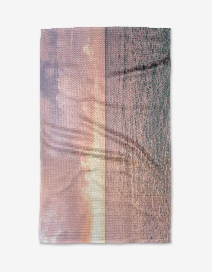 The Kait Hanson Tropical Sunrise recycled kitchen towel features a pastel ocean sunset in soft pink, orange, and purple tones across sky and water, displayed flat on a white background.
