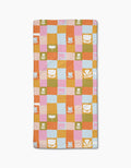 The Tulip Picnic by Lisa Nelson is a rectangular quilted blanket with orange, pink, blue, and green checkered squares, featuring white tulip and leaf motifs—crafted from post-consumer recycled materials for eco-friendly style.