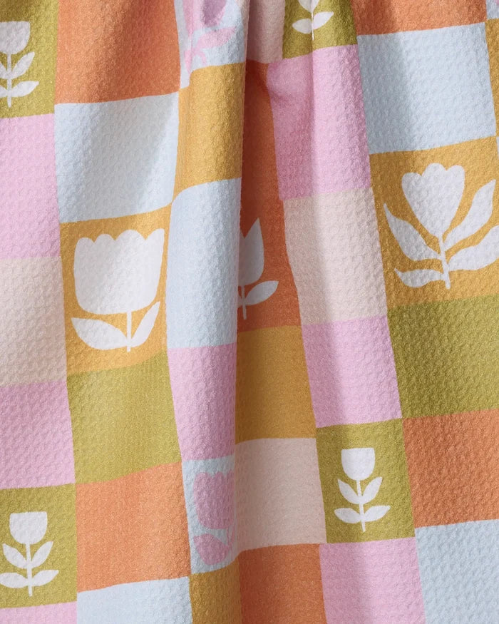 The Tulip Picnic kitchen towel by Lisa Nelson features a textured checkered pastel pink, orange, yellow, and blue design with white tulip and leaf motifs, crafted from recycled materials.