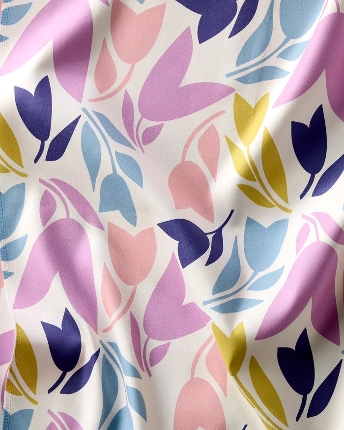 A close-up of the Tulip Tumble Dinner Napkin Set by Lizzie Clark, showing a colorful abstract floral pattern with pink, blue, yellow, and purple on white fabric with a softly wrinkled texture.