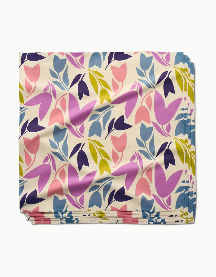 The Lizzie Clark Tulip Tumble dinner napkin features a colorful floral pattern with pink, purple, yellow, and blue leaves and flowers on cream Geosuede fabric made from recycled materials.