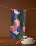 The Geometry Tumble ultra-absorbent towel with a colorful geometric pattern hangs on a clothesline with clothespins above stacked white plates and a dish brush against a brown background.