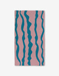 The GEOMETRY Turquoise Twist towel features a pink base with five wavy blue stripes and Geoweave technology, offering ultra-absorbency for those seeking stylish and functional Luxe Bath Towels.