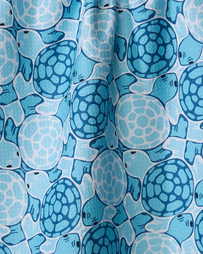 A close-up of the "Turtles" tea towel by Marta Harvey, showcasing a vibrant pattern of blue sea turtles in varied shades overlapping on a lighter blue background for striking contrast.