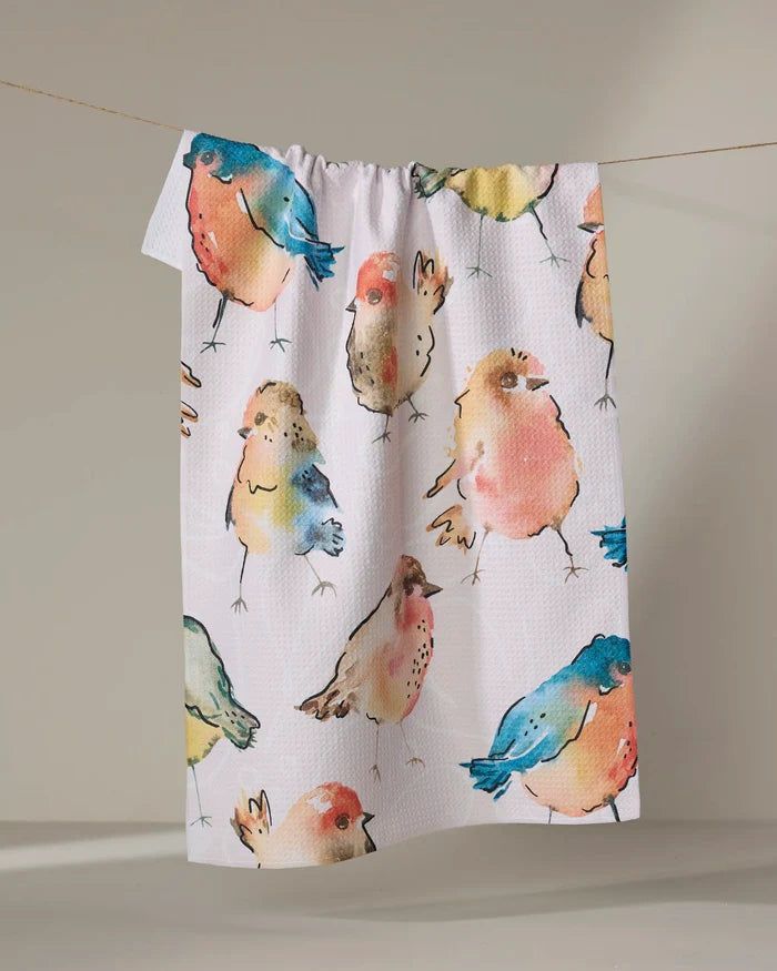 The "Tweet Tweet" tea towel by Sara Mari, in white and ultra-absorbent, features colorful watercolor-style bird illustrations and hangs on a line against a neutral background.