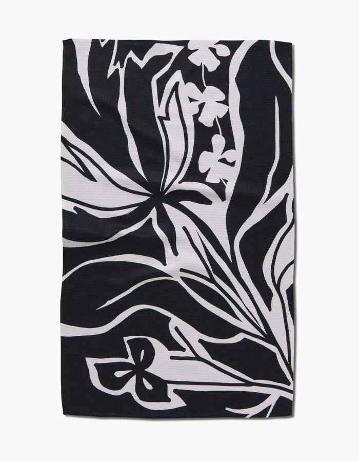 The Ash Cascade Twilight Plant is a rectangular black kitchen towel with abstract white floral and leaf patterns. Bold lines and stylized shapes create a modern, eco-friendly accent for any space.