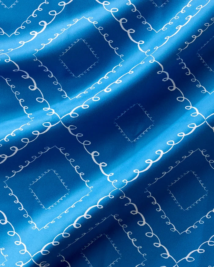 Twirls napkins by Elena Fay feature blue fabric with a white diamond pattern of swirling lines. Eco-friendly and slightly wrinkled, they add elegant light and shadow to any table setting.