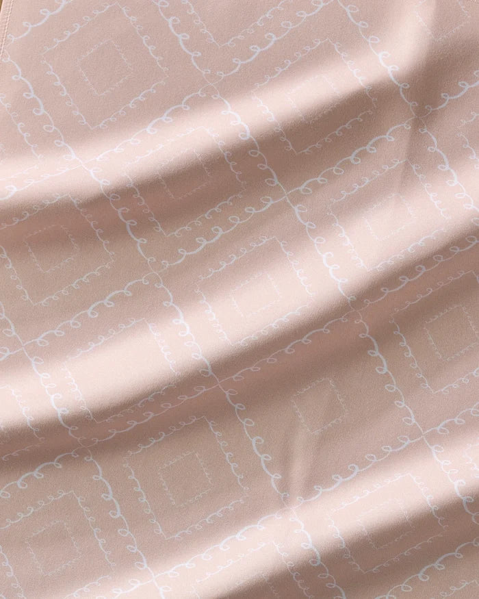 A close-up of Twirls by Elena Fay shows light pink fabric with a subtle white diamond and swirl pattern, creating a soft, delicate texture—ideal for eco-friendly or recycled dinner napkins.