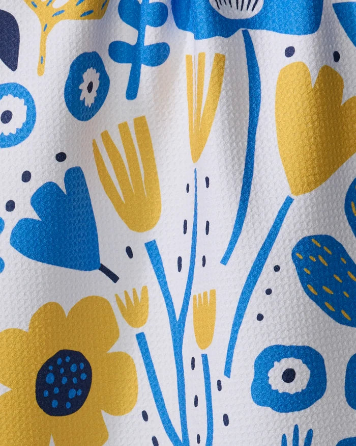 The Ukrainian Florals kitchen towel by Marina Solodka features a colorful floral pattern with yellow, blue, and dark blue flowers on a textured white background. Made from recycled materials, its playful design brings modern charm to any kitchen.