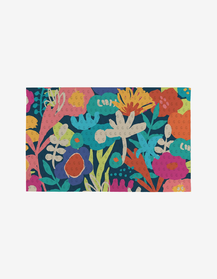 The Sareka Unique “Unique” mat is a colorful rectangular rug with abstract pink, blue, yellow, orange, and green floral patterns on a dark background, crafted from eco-friendly post-consumer recycled materials.
