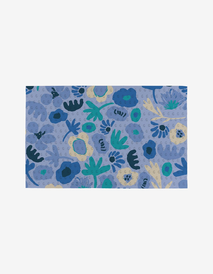 The Sareka Unique Unique mat features a blue background with an abstract floral pattern in blue, teal, cream, and green. Made from eco-friendly post-consumer recycled materials, it showcases scattered flower and leaf shapes.