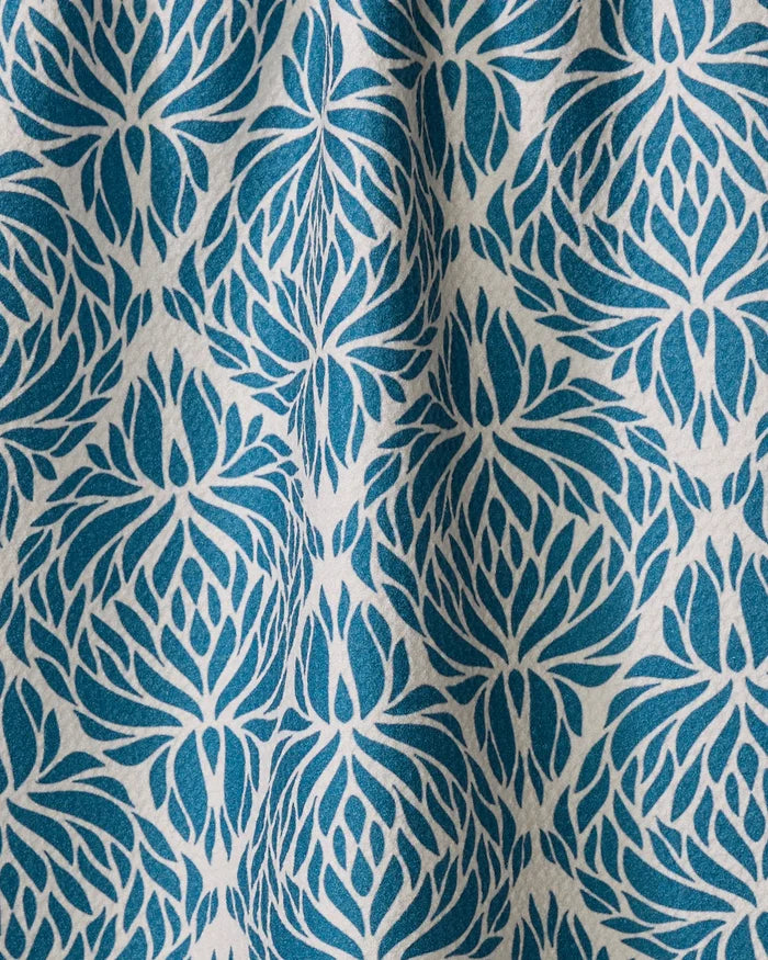 The “Untangled” tea towel by Rebecca Woolbright features a blue and white repeating floral or leaf design. Made from quick-drying recycled materials, its subtle folds and shadows provide added texture and visual depth.