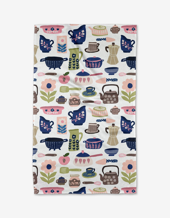The Utensils tea towel by Cottonflower Studio is made from recycled materials and displays a vibrant, playful design of teapots, cups, and kitchen items in pink, blue, green, and brown on a white background.