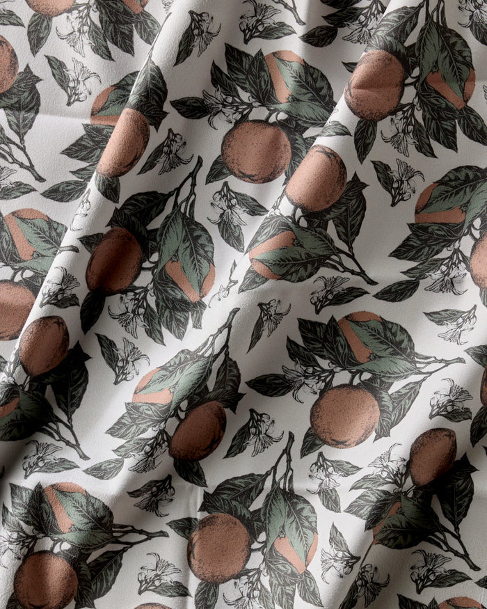Geometry’s Valencia napkins feature a botanical pattern of oranges, green leaves, and white flowers on a light background. These absorbent cloth napkins add gentle folds, shadows, and elegant texture to your dining table.