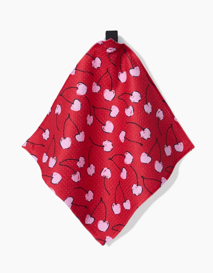 The Hufton Studio Valentines dishcloth features a super-absorbent design with a red background, pink cherries, and black stems. It hangs by a black loop against a white backdrop.