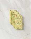 Seven yellow "Veg on Parade" reusable paper towels by Lizzie Clark, featuring a green and white vegetable print, are neatly stacked diagonally on a white marble surface.