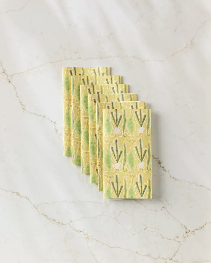 Seven yellow "Veg on Parade" reusable paper towels by Lizzie Clark, featuring a green and white vegetable print, are neatly stacked diagonally on a white marble surface.